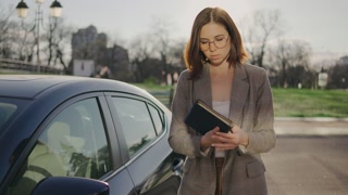 A business woman gets out of her car and opens a notebook with important notes on a business project.